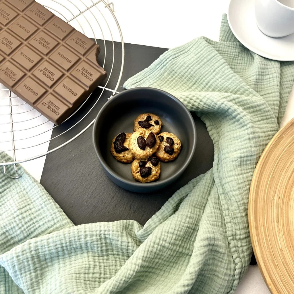 Zuckerfreie Kekse goldbraun auf unklem untergrund neben grünem tuch neben schokolade