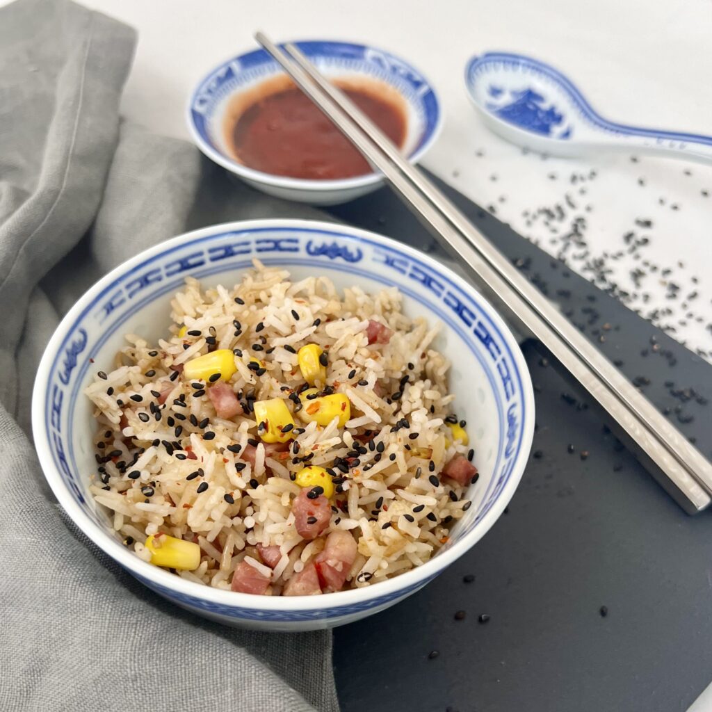 schnelle Reispfanne chinesisch - Fried Rice auf weissem untergrund mit schwarzen Sesamkörnern neben schwarzer platte mit grauem tuch