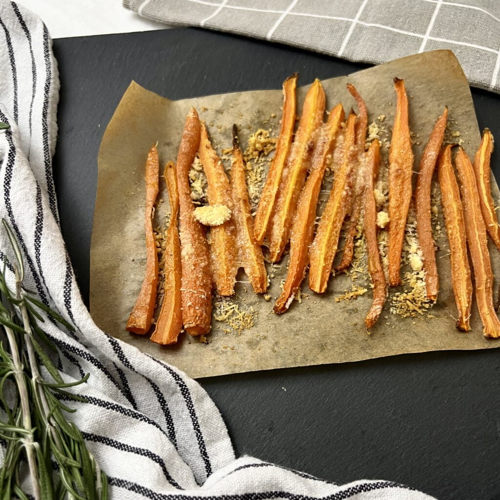 Parmesan Karotten aus dem Ofen auf dunklem untergrund neben gestreiftem weiss grauen tuch