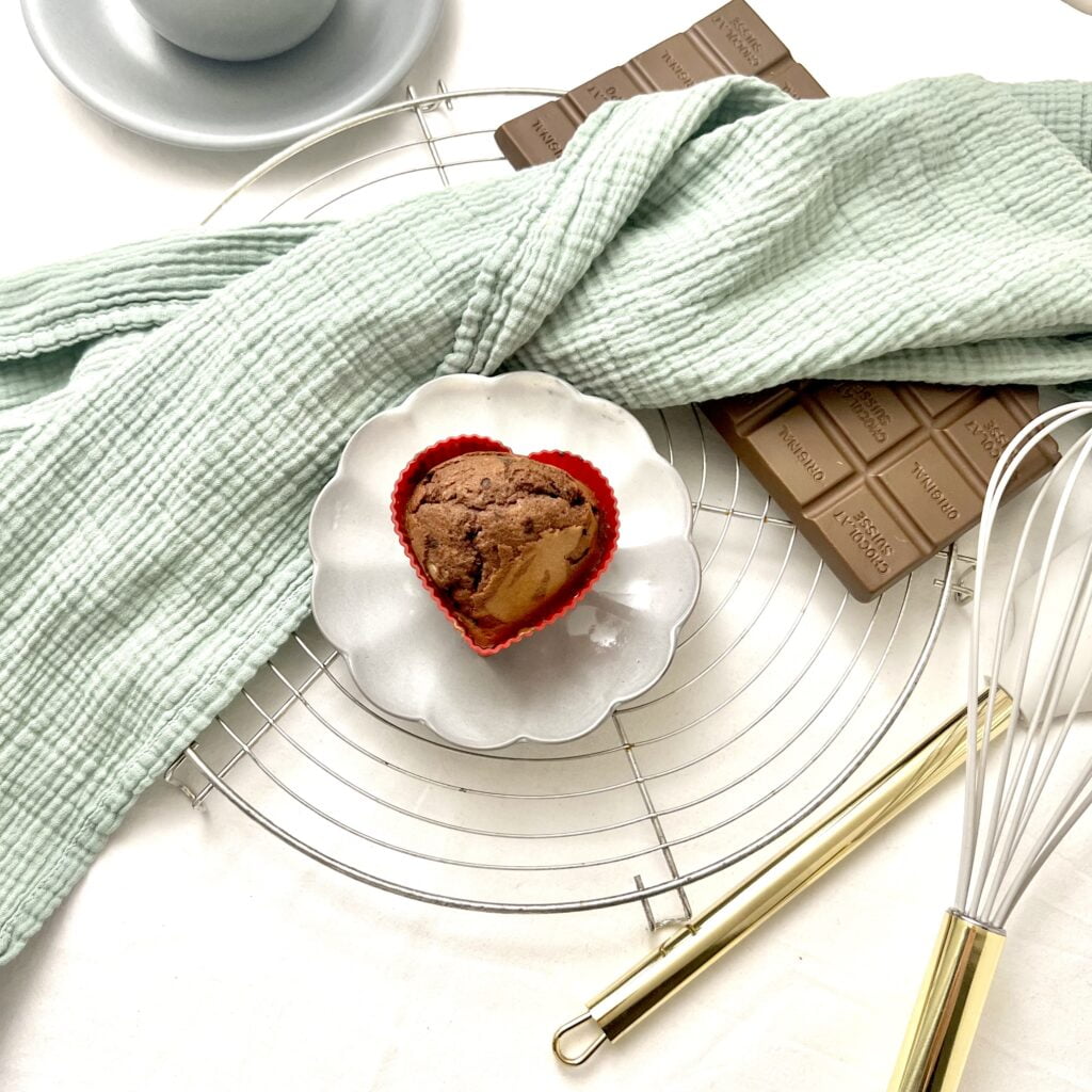 Marmor Muffins goldbraun auf grauem teller neben grünem tuch neben brauner schokolade auf weissem untergrund neben grauer tasse