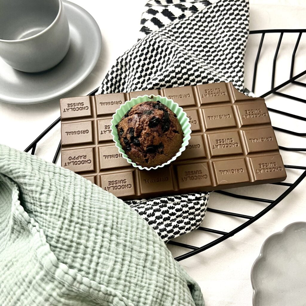 Schoko Blaubeer Muffins braun auf brauner schokoladentafel auf weiss schwarz gestreiftem Untergrund neben grünem tuch neben grauer Tasse